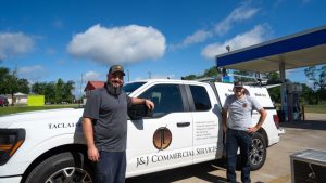 two smiling workers in front of a a white company vehicle with the J&J Commercial Services logo