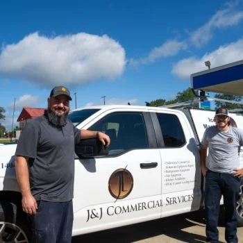 two smiling workers in front of a a white company vehicle with the J&J Commercial Services logo
